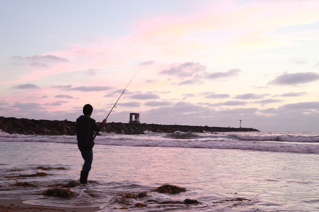 Silhouette of a person fishing while ankle deep in the water